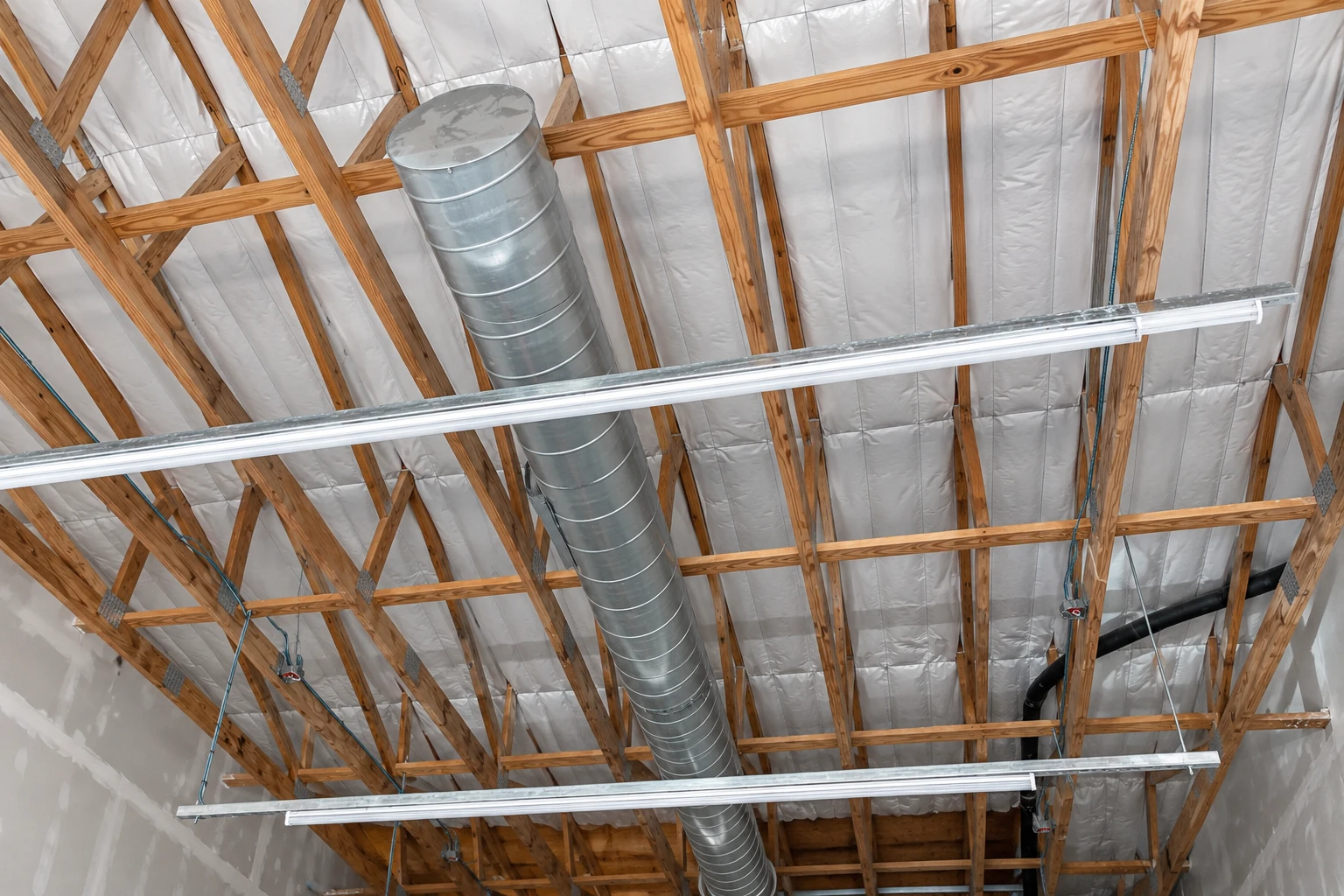 Commercial roof insulation covers the spaces between exposed wooden trusses, alongside a metal air duct and suspended lights.