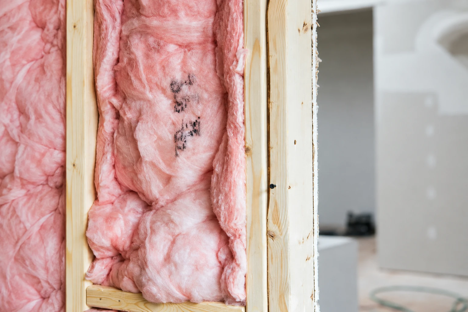 Pink fiberglass batts fill exposed wall framing, with dark marks on the insulation and a finished room visible beyond.