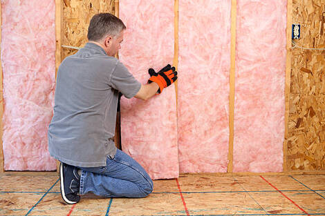 Person installing pink insulation into a wall in the basement of a home in Norwalk, CT.