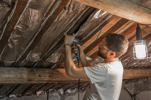 Person using a staple gun to install insulation into a Norwalk attic.