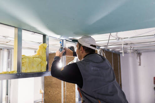 Person drilling a bracket into the ceiling to install insulation in Norwalk.